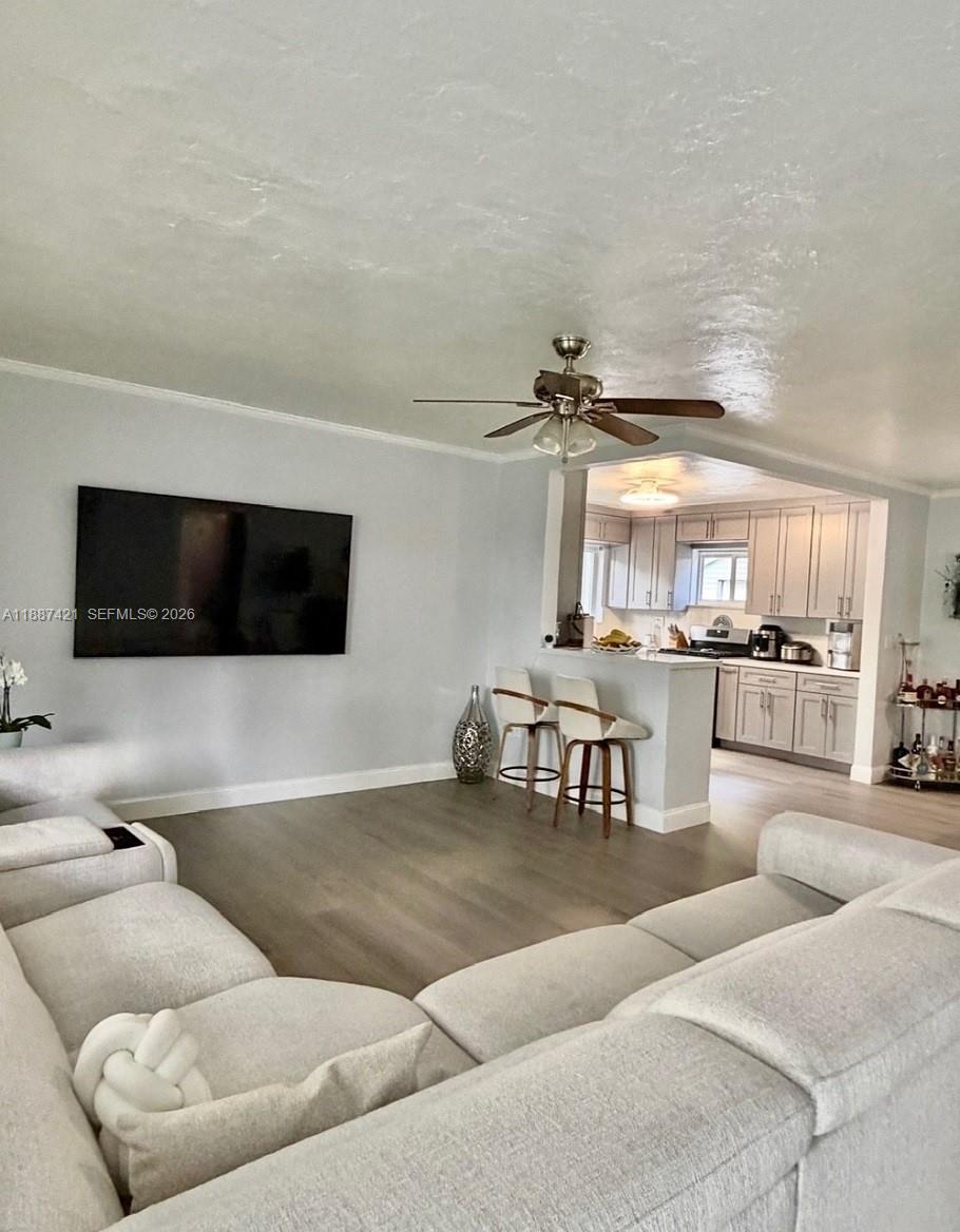 A living room with a large sectional sofa faces a wall-mounted television and open kitchen — 9021 SW 197th St, Cutler Bay FL 33157, CUTLER BAY, FL