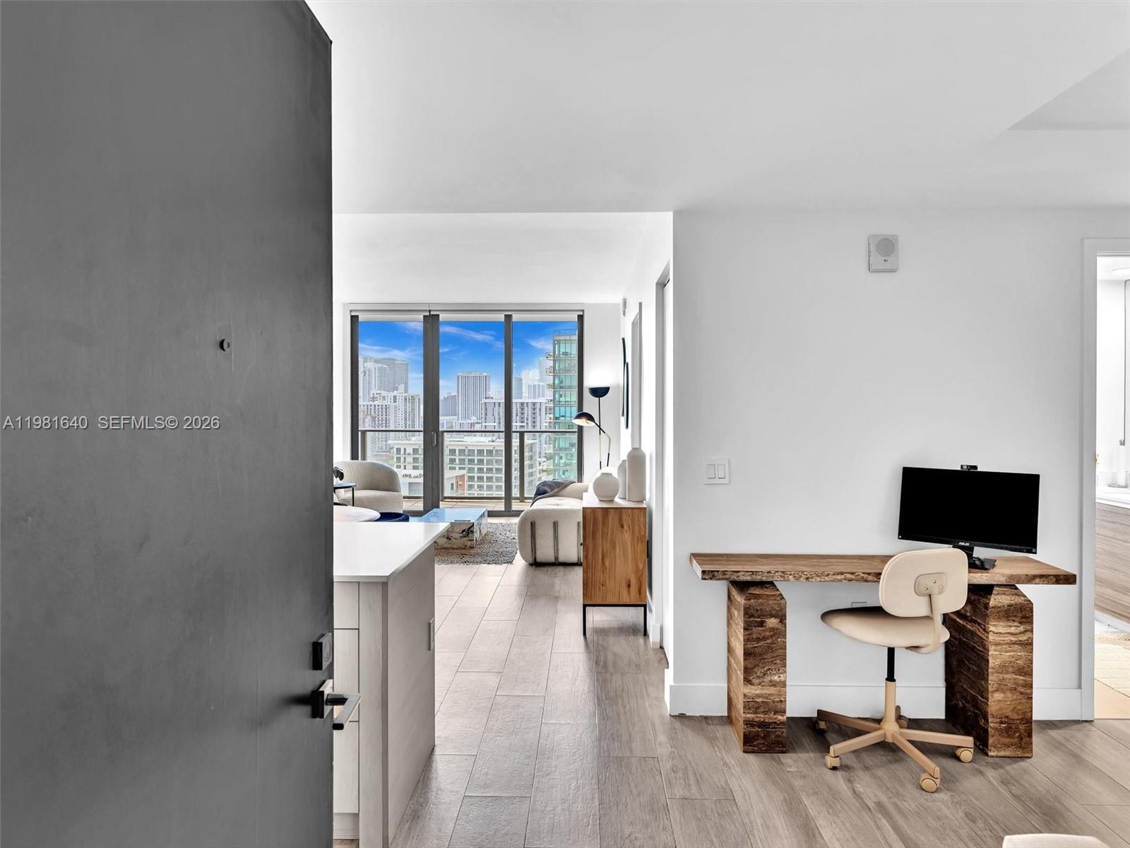 A modern apartment interior features a workspace, kitchen island, and living area with city views — 121 NE 34th St # 2102, Miami FL 33137, MIAMI, FL