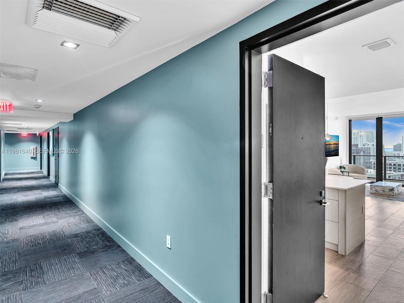 A hallway with blue walls and carpet leads to an open doorway revealing an apartment — 121 NE 34th St # 2102, Miami FL 33137, MIAMI, FL