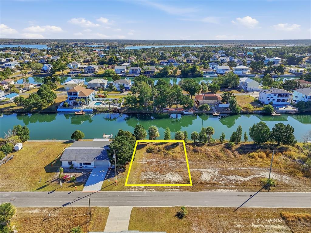 An aerial view shows a vacant, rectangular waterfront lot outlined in yellow next to a house — 3318 GARDENIA DRIVE, HERNANDO BEACH, FL