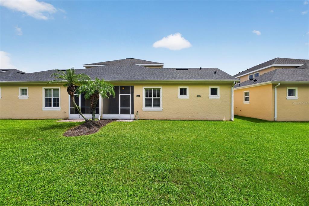 The rear exterior of a yellow house features a screened-in patio and a grassy lawn — 3421 TORRE BOULEVARD, NEW SMYRNA BEACH, FL