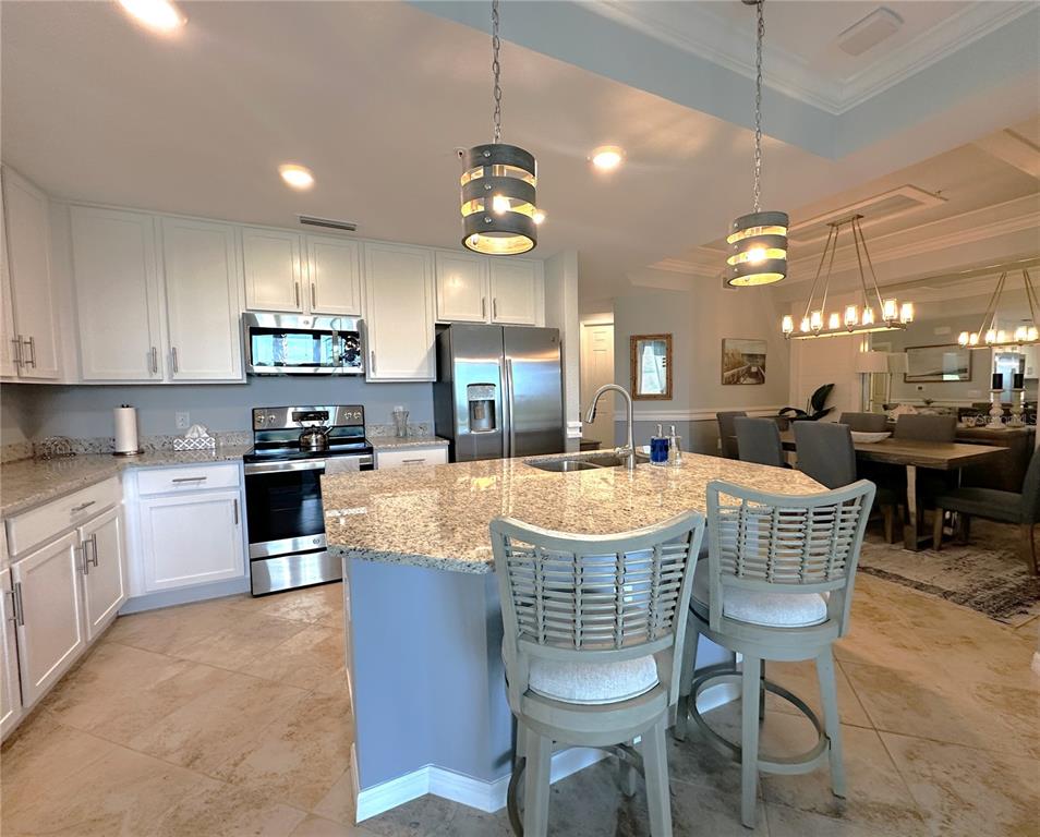 A kitchen features white cabinets, granite countertops, a central island with bar stools, and stainless appliances — 14061 HERITAGE LANDING BOULEVARD UNIT 418, PUNTA GORDA, FL