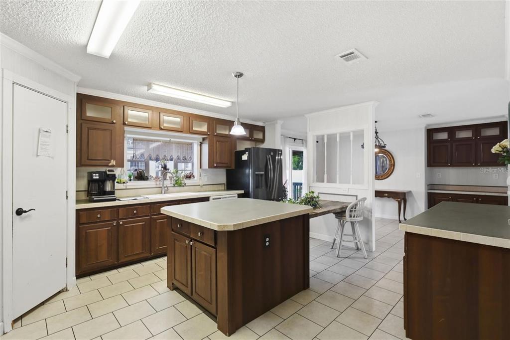 A kitchen features dark wood cabinets, a central island, and light-colored tile flooring — 8798 SW 66TH AVENUE, OCALA, FL