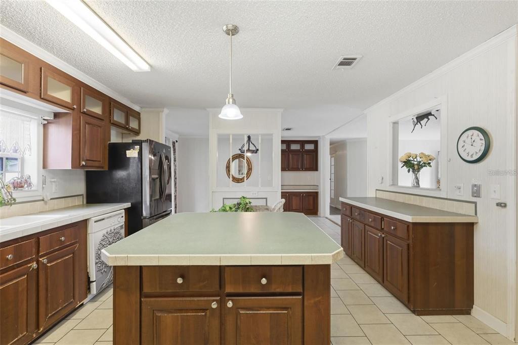 A kitchen features a central island, dark wood cabinets, and light-colored tile flooring — 8798 SW 66TH AVENUE, OCALA, FL