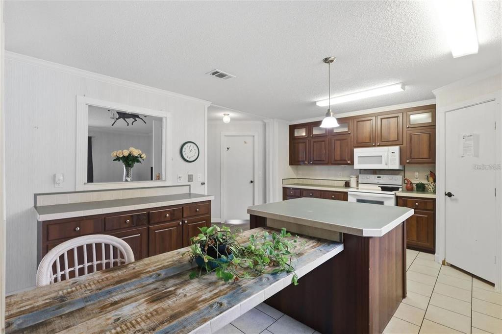 A kitchen features dark wood cabinets, a central island with a rustic table, and tile flooring — 8798 SW 66TH AVENUE, OCALA, FL