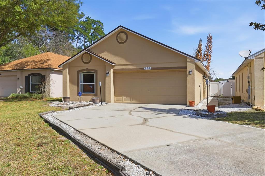 A tan single-story house with a cracked concrete driveway and a large tree in front — 138 PLACID WOODS COURT, SANFORD, FL