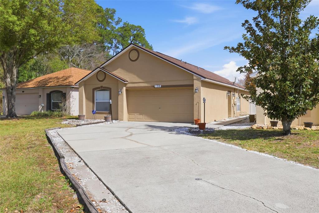 A tan single-story house with a concrete driveway and a large tree in the yard — 138 PLACID WOODS COURT, SANFORD, FL