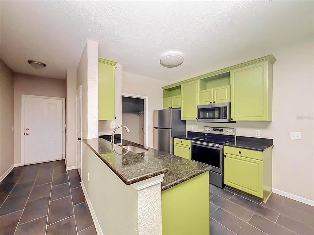 A kitchen features lime green cabinets, dark granite countertops, stainless steel appliances, and tile flooring — 6003 HEMINGWAY CIRCLE UNIT 6003, HAINES CITY, FL