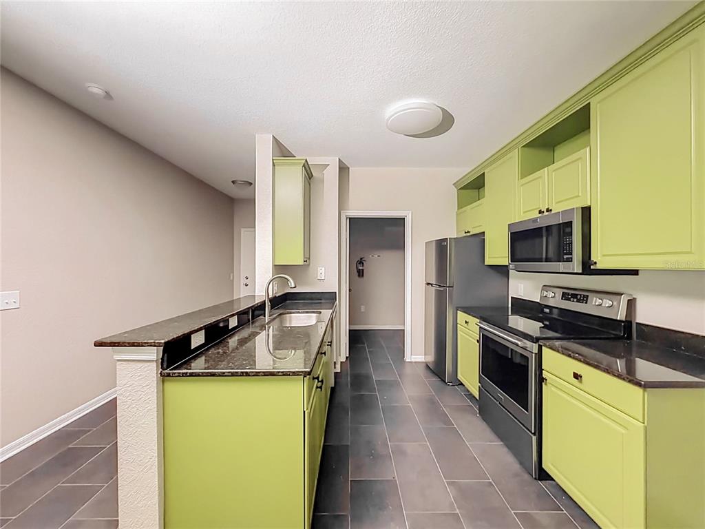A kitchen features lime green cabinets, dark granite countertops, stainless steel appliances, and tile flooring — 6003 HEMINGWAY CIRCLE UNIT 6003, HAINES CITY, FL