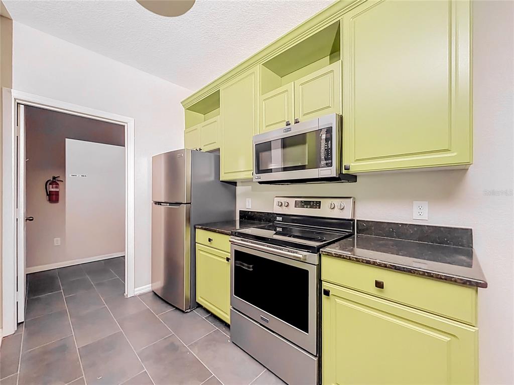 A kitchen features light green cabinets, stainless steel appliances, and dark countertops over tiled floors — 6003 HEMINGWAY CIRCLE UNIT 6003, HAINES CITY, FL