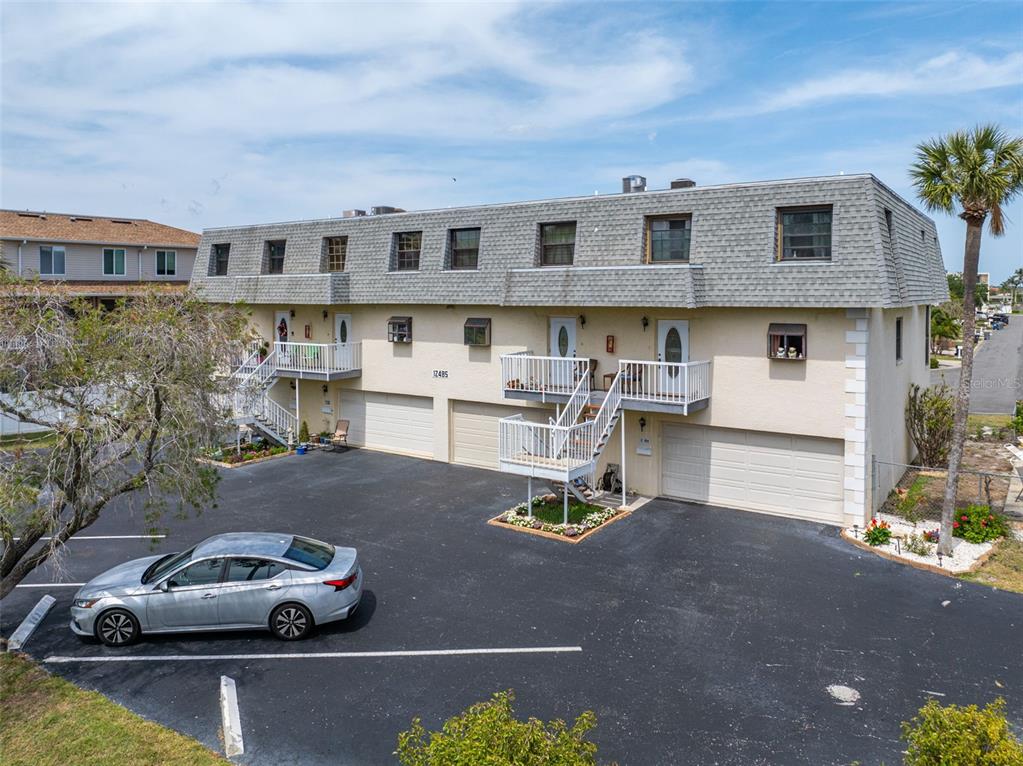 An exterior view of a multi-unit residential building with garages and elevated entry balconies — 12485 2ND STREET E UNIT C103, TREASURE ISLAND, FL