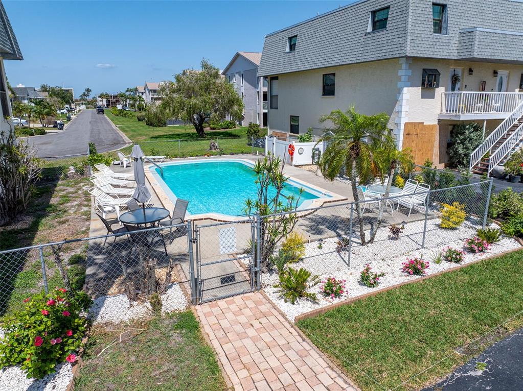 An outdoor swimming pool is enclosed by a chain-link fence next to a multi-story building — 12485 2ND STREET E UNIT C103, TREASURE ISLAND, FL