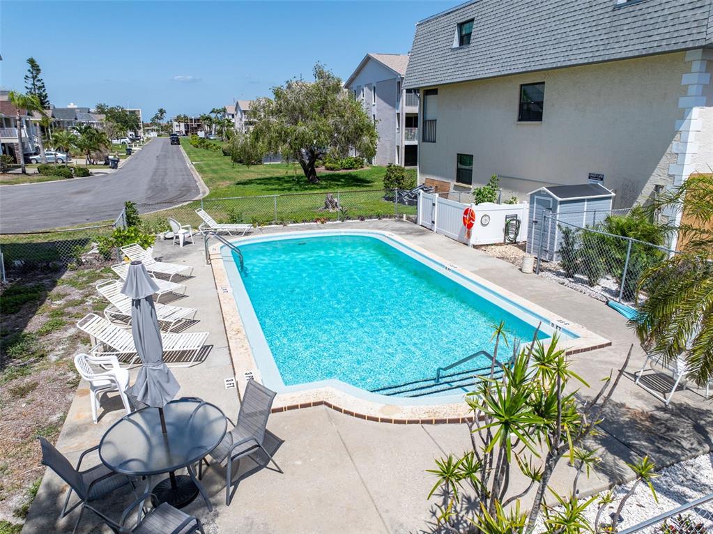 An outdoor swimming pool with lounge chairs and a patio area sits beside a building — 12485 2ND STREET E UNIT C103, TREASURE ISLAND, FL