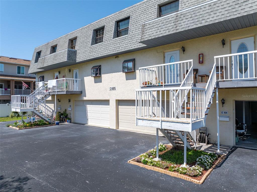 An exterior view of a multi-story apartment building with stairs leading to elevated entryways — 12485 2ND STREET E UNIT C103, TREASURE ISLAND, FL