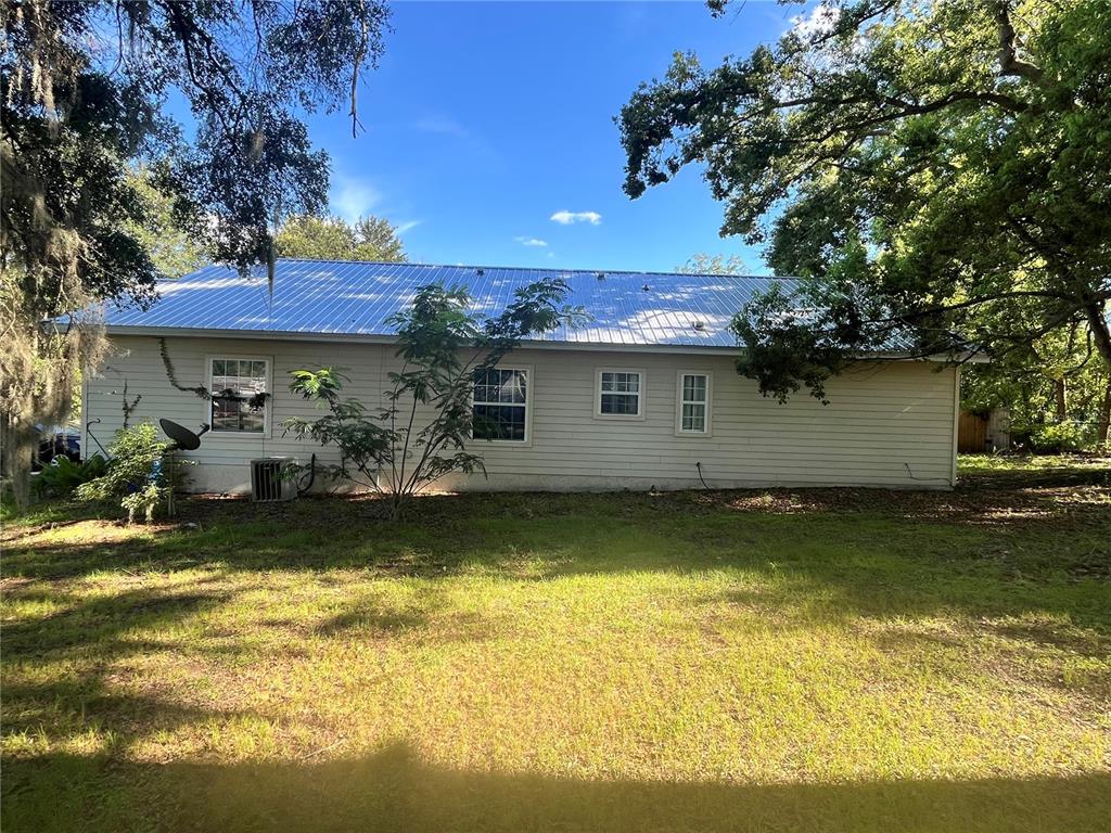 A single-story house with light-colored siding and a metal roof sits on a grassy lot — 15704 NW 140TH STREET, ALACHUA, FL