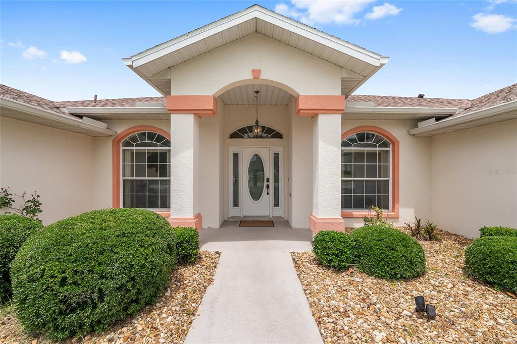 The front exterior of a house features a covered entryway with white columns and landscaping — 8598 SW 56TH AVENUE ROAD, OCALA, FL