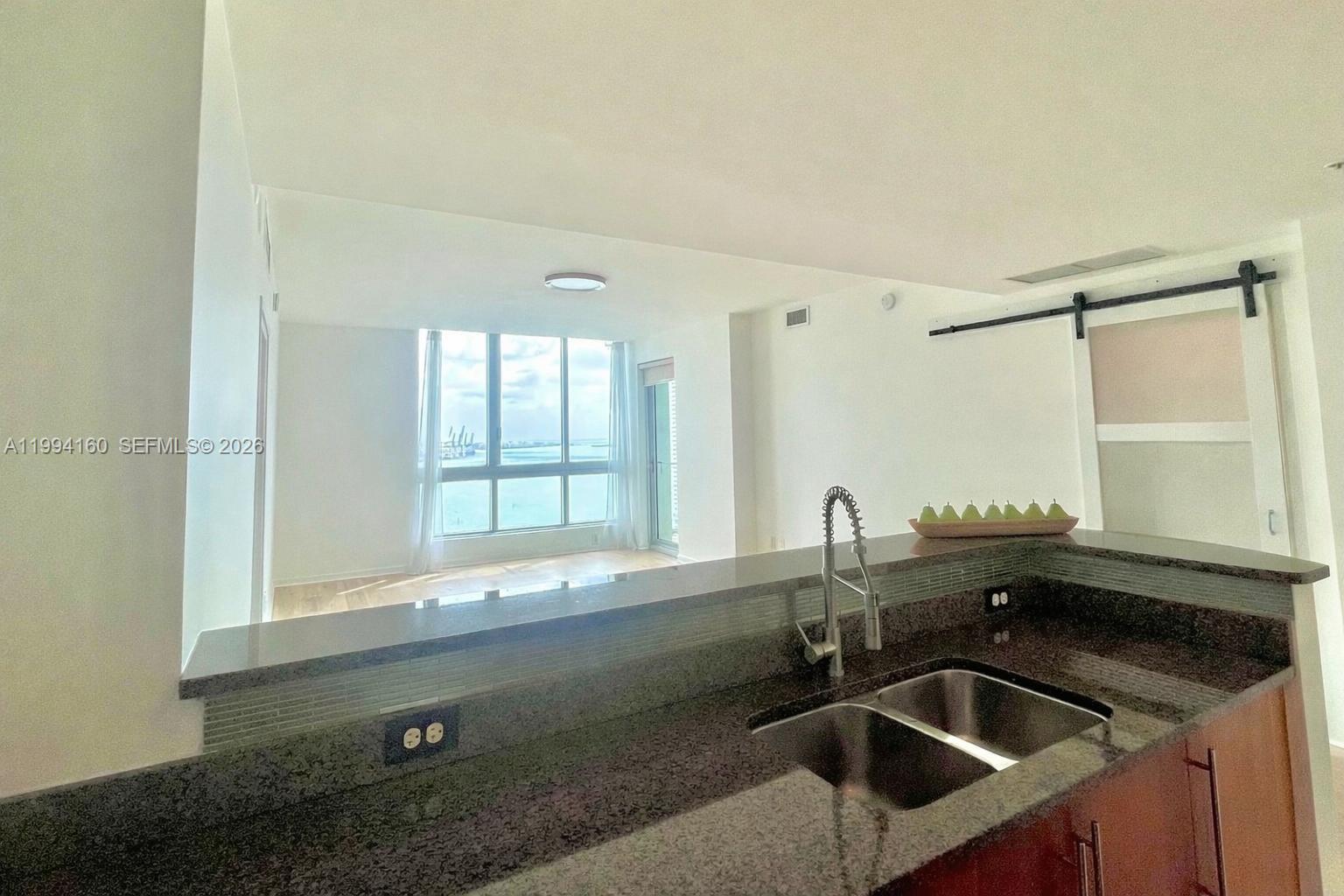 A kitchen with dark granite countertops and a double sink overlooks a bright living area — 300 S Biscayne Blvd # 2012, Miami FL 33131, MIAMI, FL