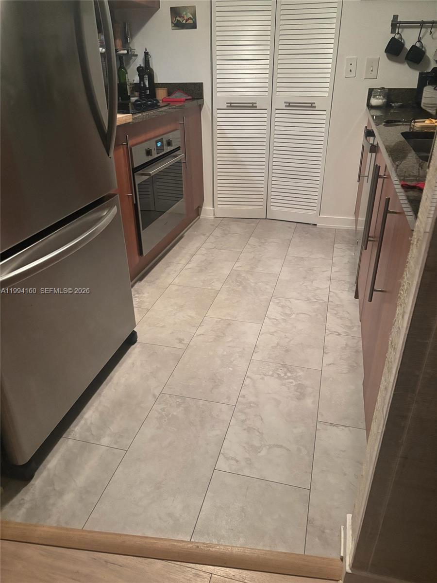 This galley kitchen features stainless steel appliances, wood-toned cabinetry, dark countertops, and light-colored tile flooring — 300 S Biscayne Blvd # 2012, Miami FL 33131, MIAMI, FL