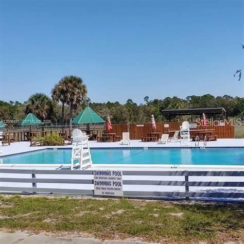 A swimming pool with a white fence and umbrellas is surrounded by trees and fencing — 580 S JASMINE STREET, CLEWISTON, FL