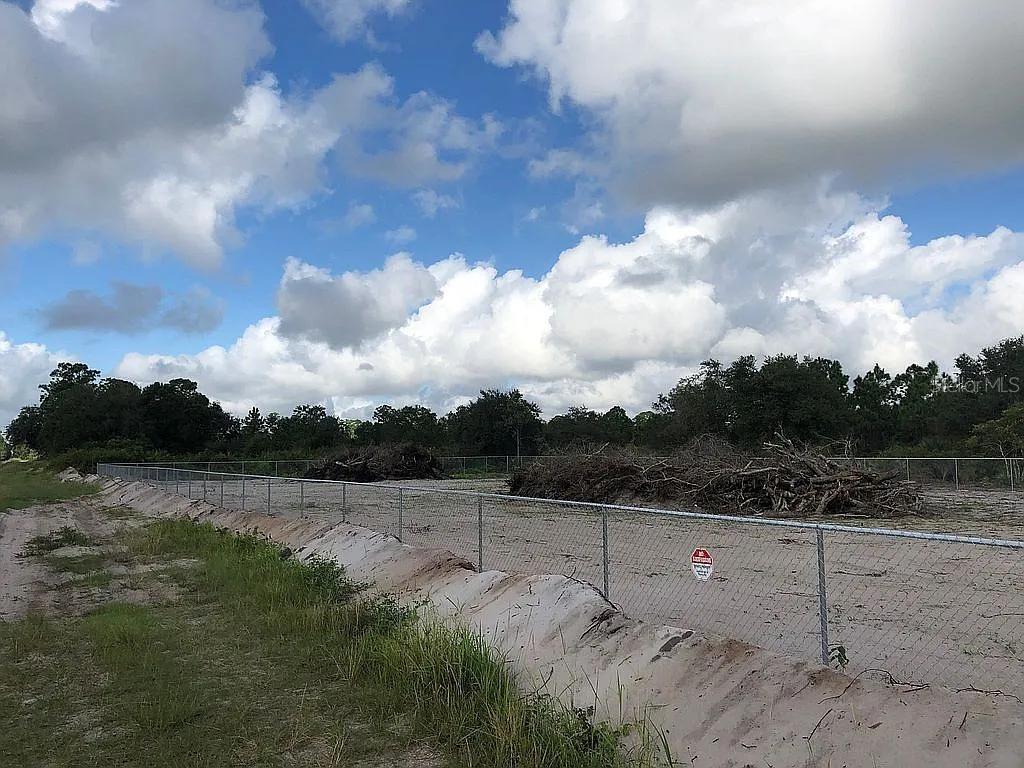 A fenced, cleared dirt lot features piles of brush under a cloudy blue sky — 580 S JASMINE STREET, CLEWISTON, FL