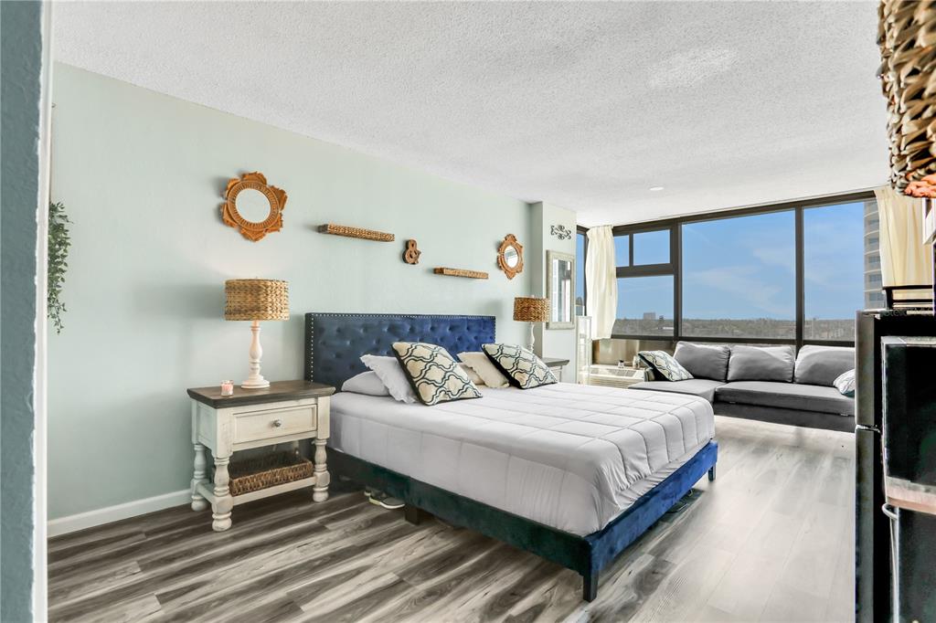 A bedroom features a blue tufted bed, a nightstand, and a sofa near large windows — 1909 S ATLANTIC AVENUE UNIT 501, DAYTONA BEACH, FL