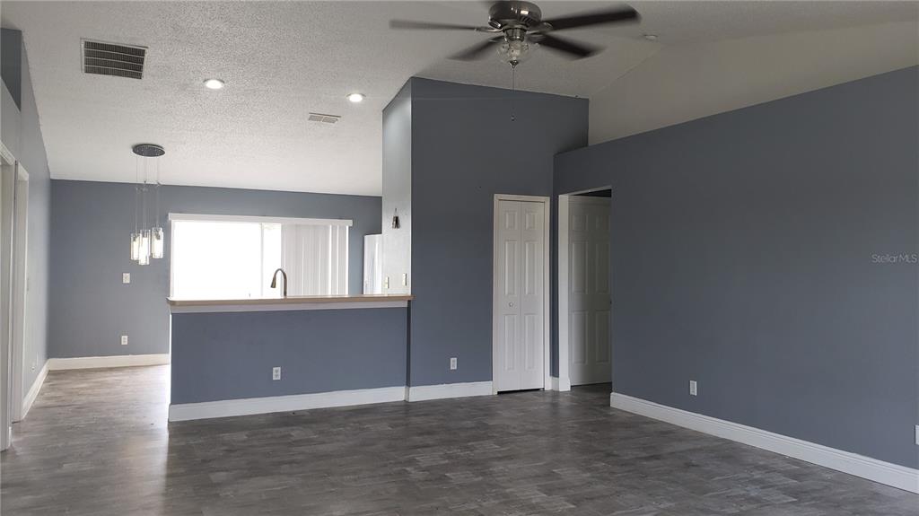 A living room with gray walls, wood-look flooring, a ceiling fan, and an open kitchen — 5141 PINE NEEDLE DRIVE, MASCOTTE, FL