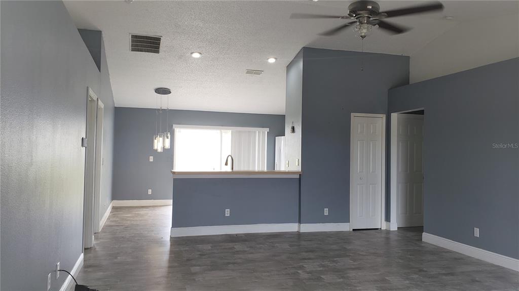 A living room with gray walls, wood-look flooring, a ceiling fan, and a kitchen pass-through — 5141 PINE NEEDLE DRIVE, MASCOTTE, FL