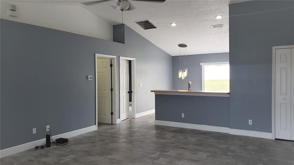 A living room with gray walls, wood-look flooring, a vaulted ceiling, and a kitchen pass-through — 5141 PINE NEEDLE DRIVE, MASCOTTE, FL