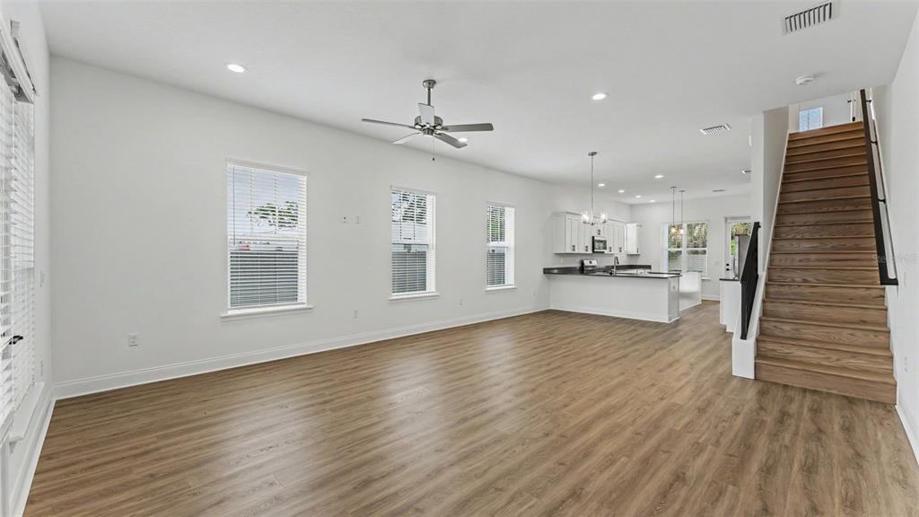 An open-concept living room features wood-look flooring, a ceiling fan, and a wooden staircase — 1031 E LIME STREET, LAKELAND, FL