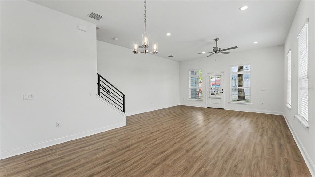 An empty room features white walls, wood-look flooring, a staircase, a chandelier, and ceiling fan — 1031 E LIME STREET, LAKELAND, FL