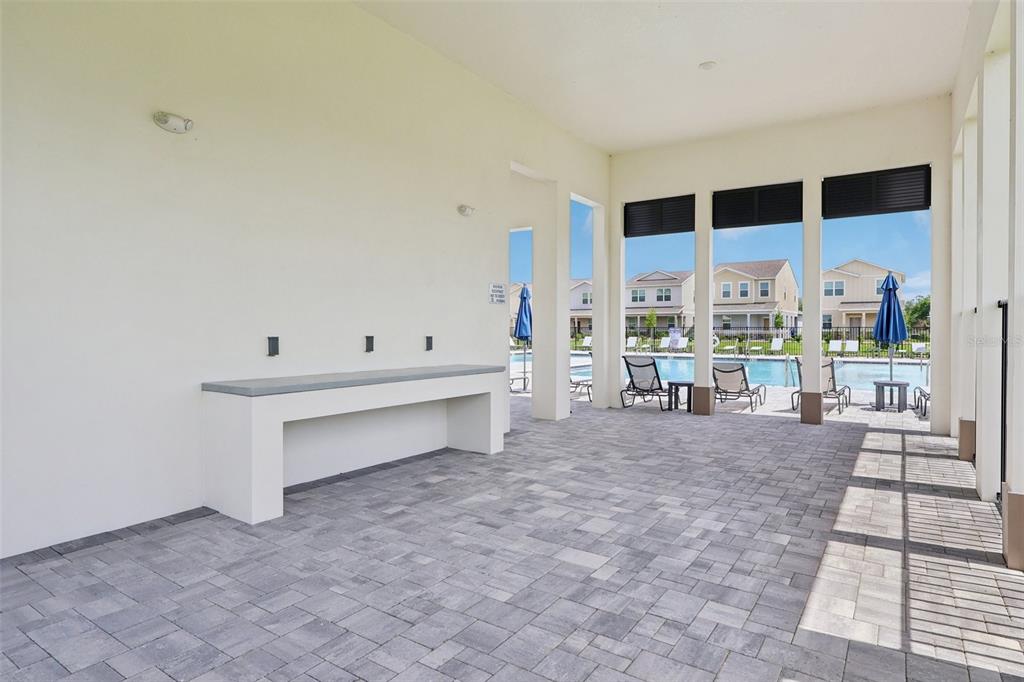 A covered outdoor patio features a stone-topped counter, paved flooring, and views of a swimming pool — 1807 LATTICE WAY, ST CLOUD, FL