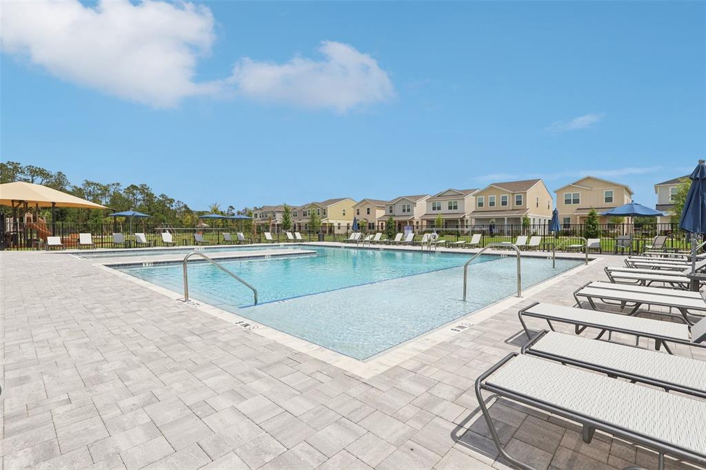 A community swimming pool with lounge chairs on a paved deck under a blue sky — 1807 LATTICE WAY, ST CLOUD, FL
