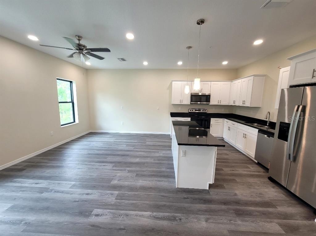 An open-concept kitchen and living area features white cabinets, black countertops, and wood-look flooring — 4351 CAMBIO GARDENS COURT, TAMPA, FL