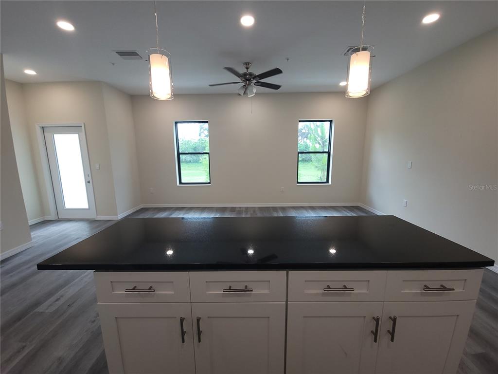 A kitchen island with a black countertop sits in front of a room with windows — 4351 CAMBIO GARDENS COURT, TAMPA, FL