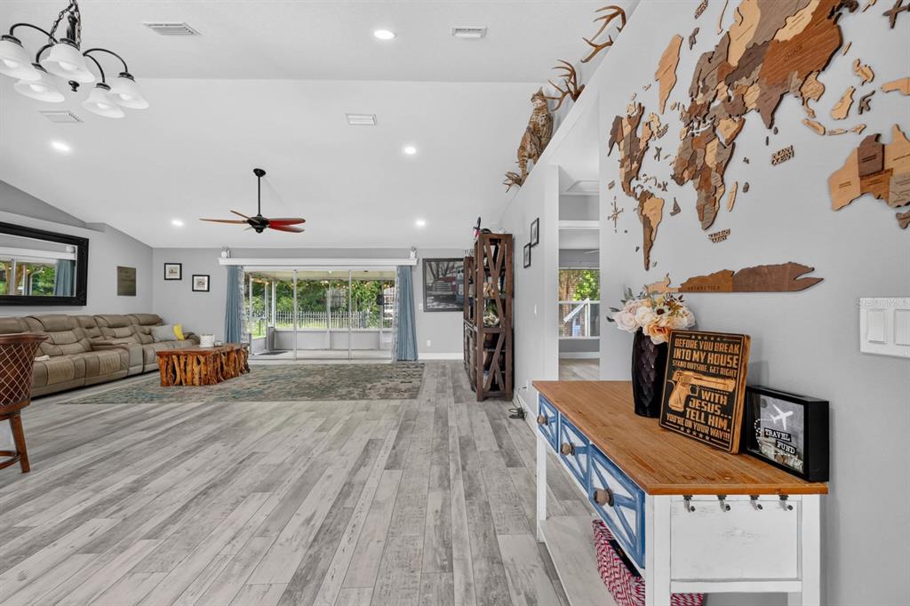 A spacious living room features light wood-look flooring, a large wall map, and sliding glass doors — 5480 SAINT REGIS WAY, PORT ORANGE, FL