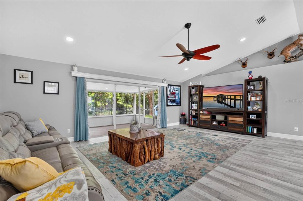 A living room features a wooden stump coffee table, a large television, and vaulted ceilings — 5480 SAINT REGIS WAY, PORT ORANGE, FL