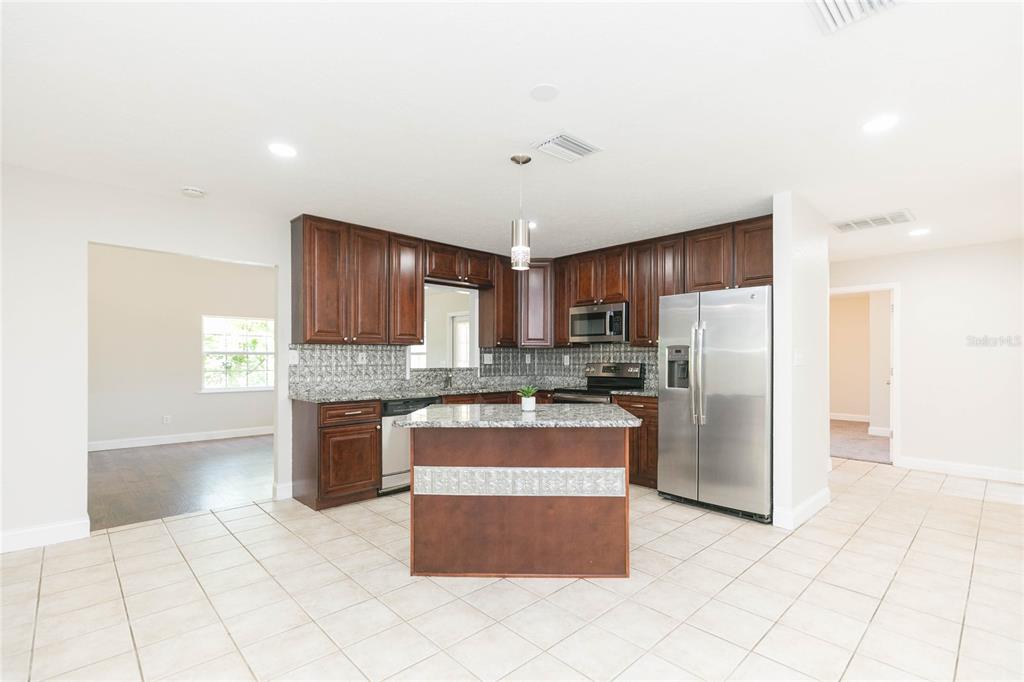 A kitchen features dark wood cabinets, granite countertops, a center island, and stainless steel appliances — 13410 LEE STREET, DADE CITY, FL