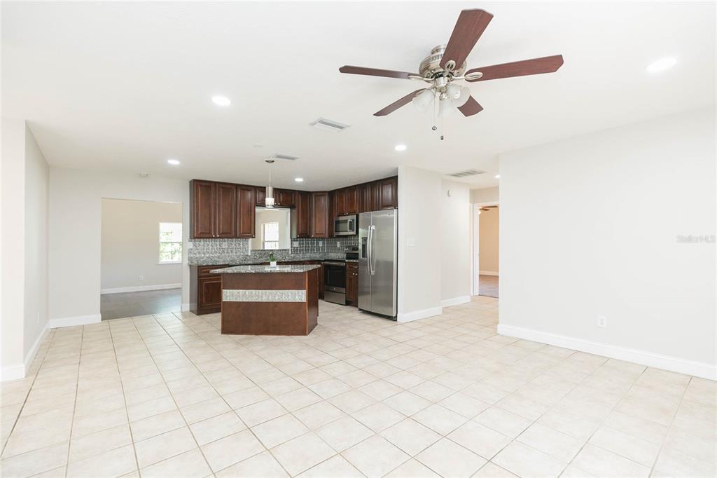 A kitchen with dark wood cabinets, granite countertops, and a center island opens to a room — 13410 LEE STREET, DADE CITY, FL