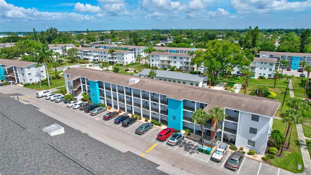 An aerial view shows a multi-story apartment complex with a parking lot and surrounding landscaping — 2217 SUNSET DRIVE UNIT E27, BRADENTON, FL