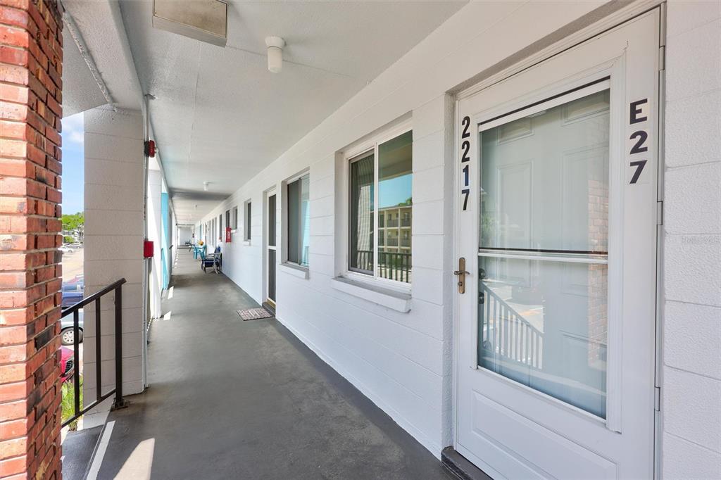 An exterior walkway leads past several white doors and windows of a multi-story apartment building — 2217 SUNSET DRIVE UNIT E27, BRADENTON, FL