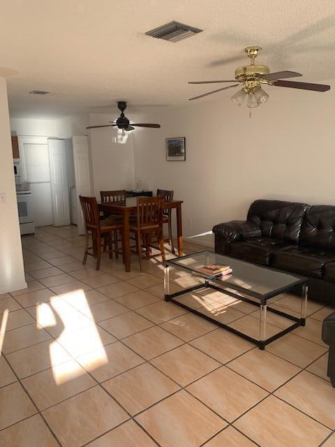 An open-concept living and dining area features tiled floors, a dark leather sofa, and ceiling fans — 933 Francis Street, West Palm Beach FL 33405, WEST PALM BEACH, FL