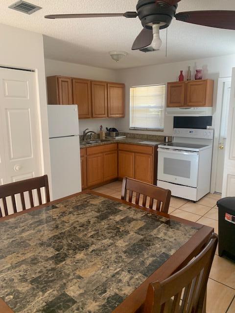A kitchen features wood cabinets, a white refrigerator, a white stove, and a dining table — 933 Francis Street, West Palm Beach FL 33405, WEST PALM BEACH, FL