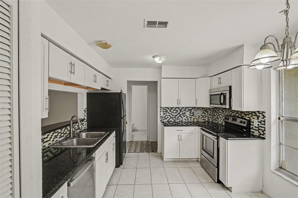 A kitchen with white cabinets, black countertops, a tiled backsplash, and stainless steel appliances — 7774 BARBERRY DRIVE, ORLANDO, FL