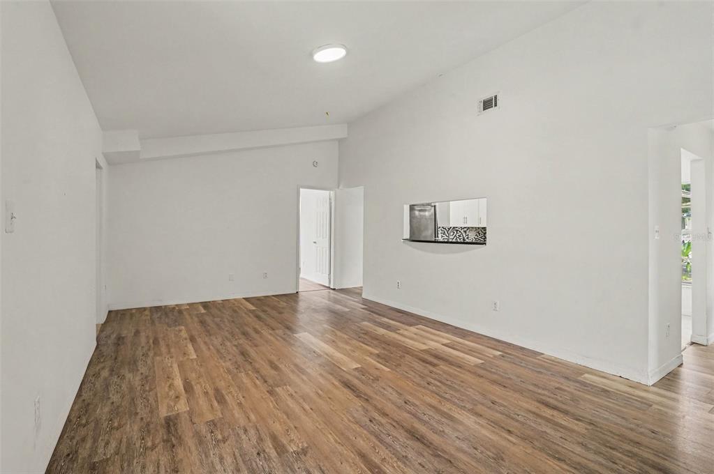 An empty room with wood-look flooring, white walls, and a kitchen pass-through window — 7774 BARBERRY DRIVE, ORLANDO, FL