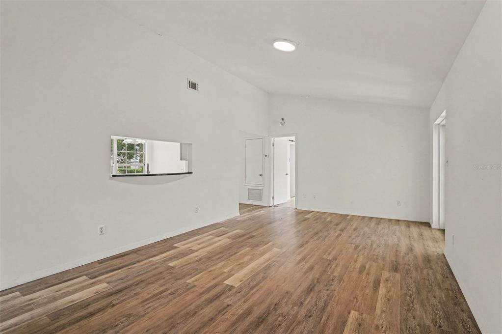 An empty room with white walls, vaulted ceilings, and wood-look flooring features a pass-through window — 7774 BARBERRY DRIVE, ORLANDO, FL