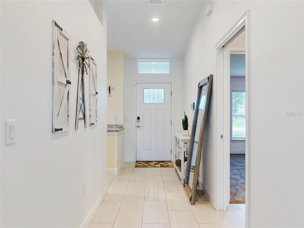 A bright entryway features white walls, tiled flooring, a front door, and decorative wall art — 2684 SHIPROCK COURT, DELTONA, FL