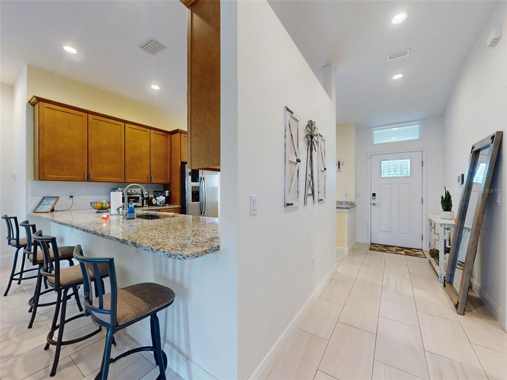 A kitchen with granite countertops and bar seating overlooks a tiled entryway with a door — 2684 SHIPROCK COURT, DELTONA, FL
