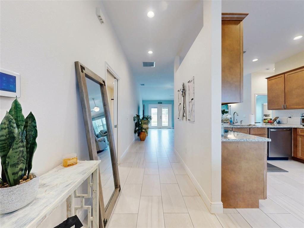 A hallway with white tile floors leads toward a doorway, flanked by a kitchen area — 2684 SHIPROCK COURT, DELTONA, FL