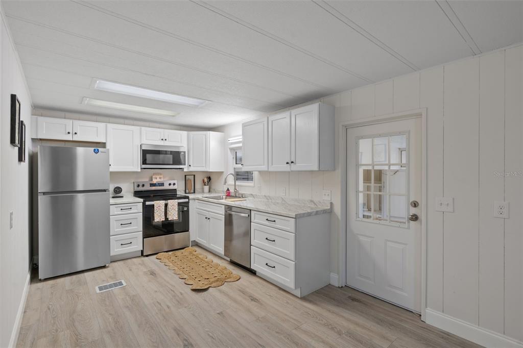 A kitchen features white cabinets, stainless steel appliances, wood-look flooring, and a glass-paneled exterior door — 3450 OSAGE DRIVE, ZEPHYRHILLS, FL