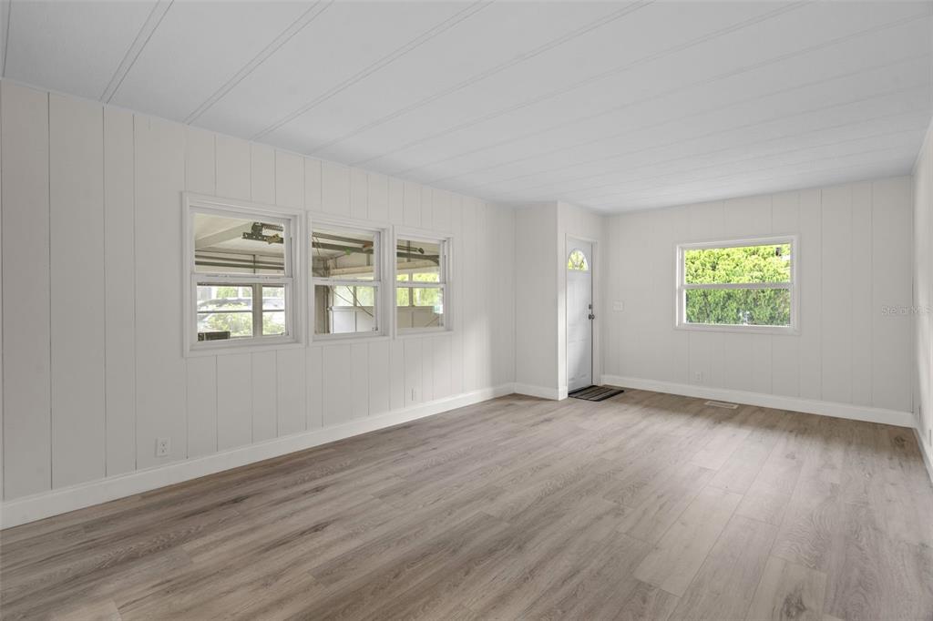 An empty room with white paneled walls, light wood-look flooring, and several windows — 3450 OSAGE DRIVE, ZEPHYRHILLS, FL